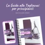 Copertina dell'eBook 'La Guida alla Tagliacuci per principianti'. L'immagine mostra una macchina tagliacuci su sfondo viola, con l'eBook visualizzato sia su un dispositivo mobile che su un blocco notes spiralato. Il titolo recita: 'La guida base (che più base non si può) alla tagliacuci'.